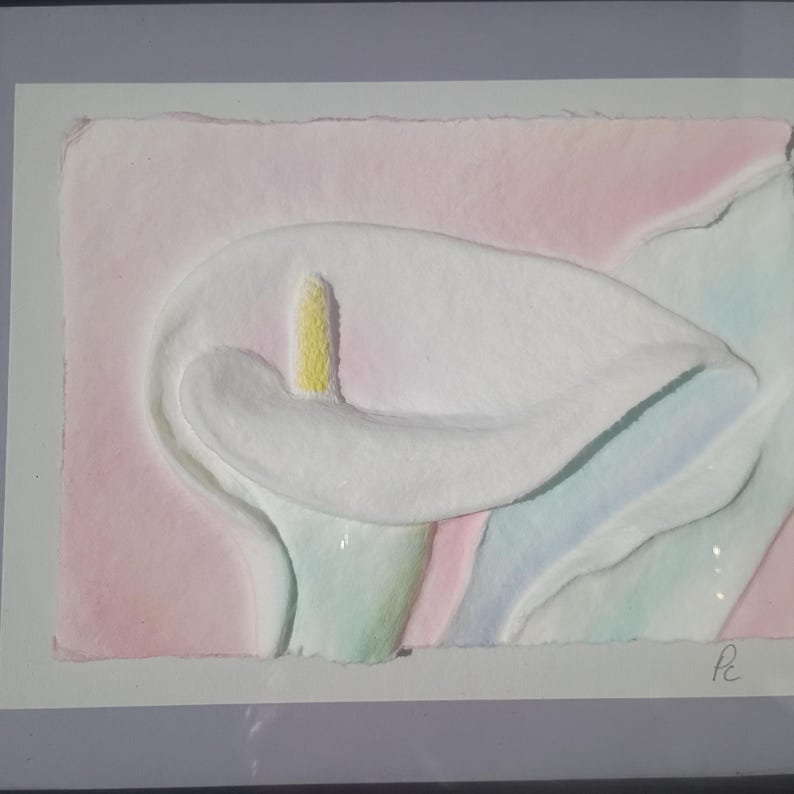 May include: A textured paper art piece featuring a white calla lily with a yellow spadix, set against a soft pink background with subtle blue and green watercolor washes. The artwork is signed with the initials Pc in the bottom right corner.