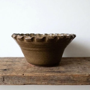 May include: A ceramic bowl with a deep olive-brown glaze and a distinctive ruffled, scalloped edge. The bowl features a wide, flared opening that tapers down to a smaller base, showcasing a smooth, glossy finish on the exterior surface.
