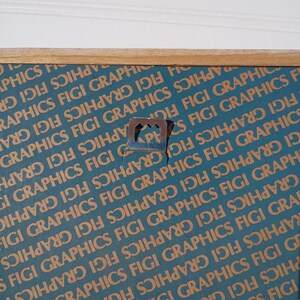 May include: Close-up of a picture frame with a teal and brown patterned background. The frame has a wooden border and a metal sawtooth hanger attached to the back for wall mounting. The background has the text "GRAPHICS FIGI" repeated.