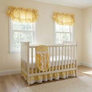 May include: A white crib with a yellow floral-patterned bumper, skirt, and matching window valances. The nursery has a light, airy feel with natural light from the windows. The crib is the focal point of the room.