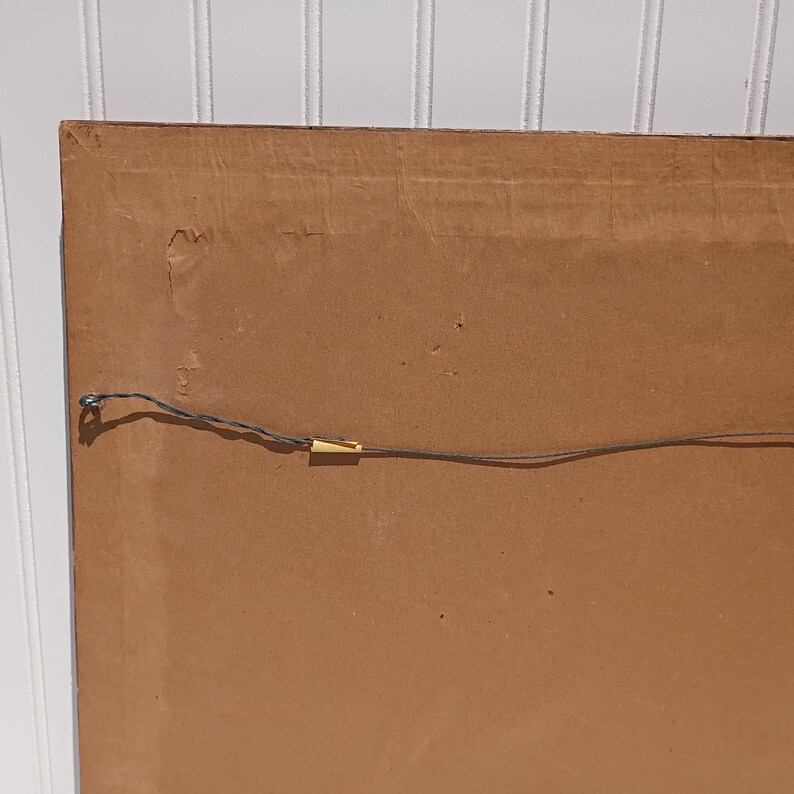 Op de afbeelding: De achterkant van een ingelijst kunstwerk, met een bruine kartonnen achterkant. Een dunne draad is over de achterkant gespannen om op te hangen. De hoek van de lijst is zichtbaar en toont de constructie.