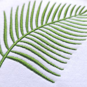 May include: A green embroidered palm leaf design on a white fabric background.