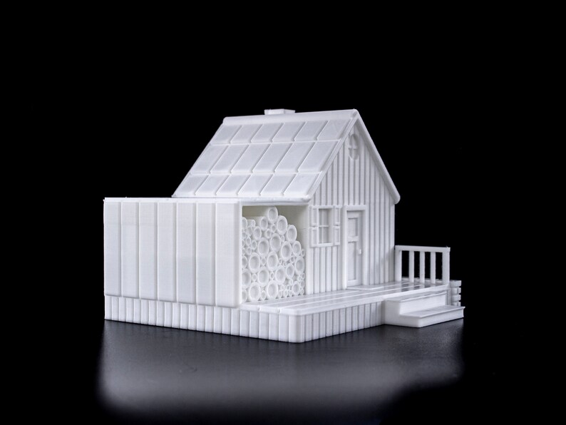 May include: A white 3D printed model of a small house with a wood-like texture. The house has a roof, a door, a window, and a small porch. There is a stack of logs next to the house.