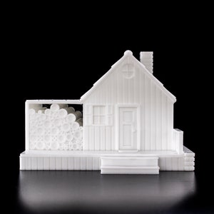 May include: White 3D printed model of a small house with a woodpile on the side. The house has a door, a window, and a chimney. The woodpile is stacked high and is made of small, round logs.