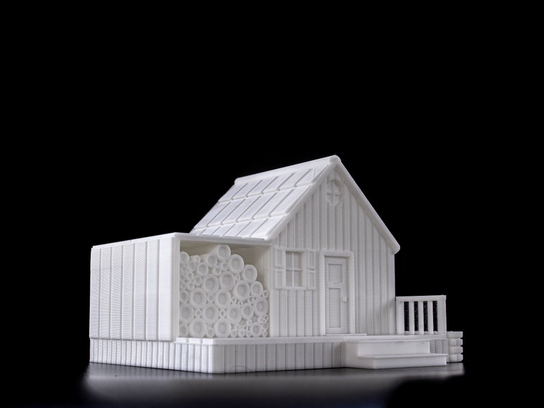 May include: A white 3D printed model of a small house with a wood-like texture. The house has a roof, a door, a window, and a porch. There is a pile of logs next to the house.