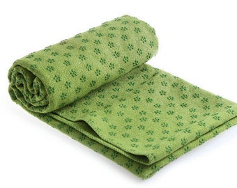 May include: A green yoga mat towel with a small, repeating pattern. The towel is rolled up and partially unrolled, showing the texture of the fabric.