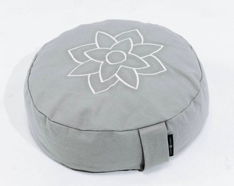 May include: A round, gray meditation cushion with a white embroidered lotus flower design. The cushion is made of a soft fabric and has a small fabric loop on the side. The cushion is designed for meditation and yoga.