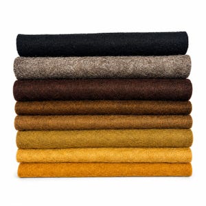 May include: A stack of eight rectangular felt sheets arranged in a gradient from black at the top, transitioning through shades of grey, dark brown, medium brown, light brown, ochre, and golden yellow at the bottom, featuring a dense, fibrous texture.