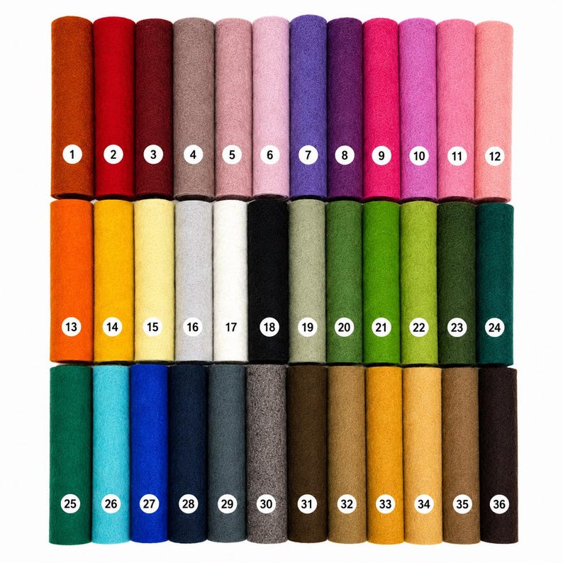May include: A collection of thirty-six cylindrical rolls of felt fabric arranged in three rows of twelve. Each roll is a distinct solid color, ranging from warm reds and oranges to cool blues, greens, and neutrals, each labeled with a white numbered circle.