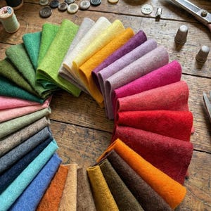May include: A collection of rectangular felt fabric swatches arranged in a circular fan pattern, featuring a wide spectrum of colours including shades of green, yellow, orange, purple, pink, red, blue, brown, and grey with a textured surface.