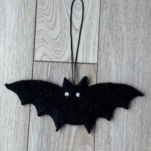 以下が含まれることがあります： 白い丸い目と黒い吊り下げ紐が付いた、黒いフェルトのコウモリの飾り。 コウモリは翼を広げ、耳が尖っています。 ハロウィーンの装飾です。