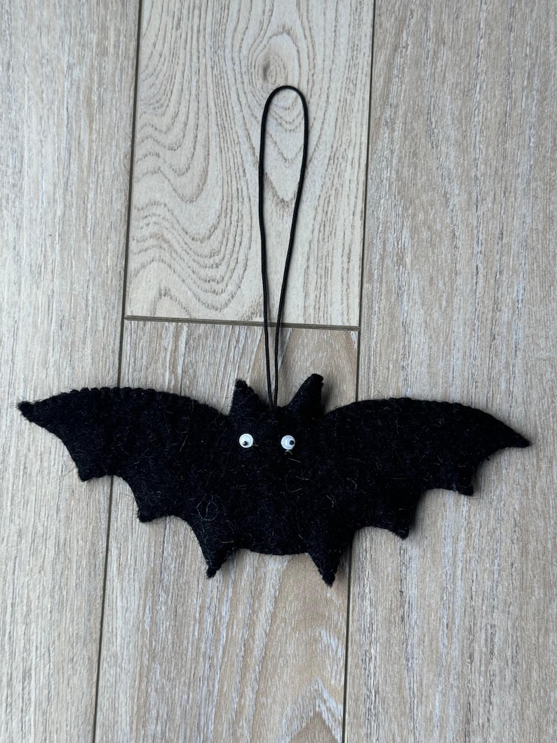 以下が含まれることがあります： 白い丸い目と黒い吊り下げ紐が付いた、黒いフェルトのコウモリの飾り。 コウモリは翼を広げ、耳が尖っています。 ハロウィーンの装飾です。