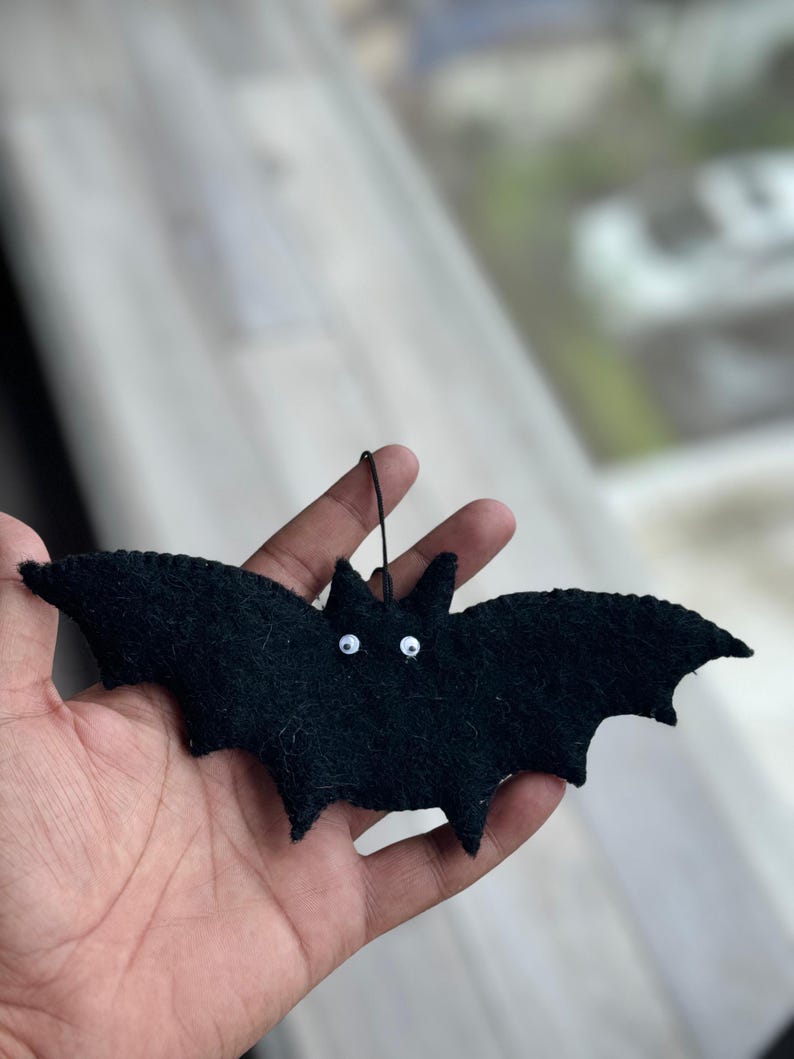 以下が含まれることがあります： 白い丸い目を持つ黒いフェルトのコウモリの飾り。 コウモリは尖った耳と吊り下げ用の紐が付いています。 羽は大きく広げられており、全体的なデザインはシンプルで、ハロウィーンの装飾に最適です。