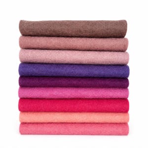 May include: A vertical stack of ten rectangular felt sheets in a gradient of colors, ranging from dark brown at the top, transitioning through shades of mauve, purple, and magenta, to a bright pink at the bottom, all featuring a textured surface.