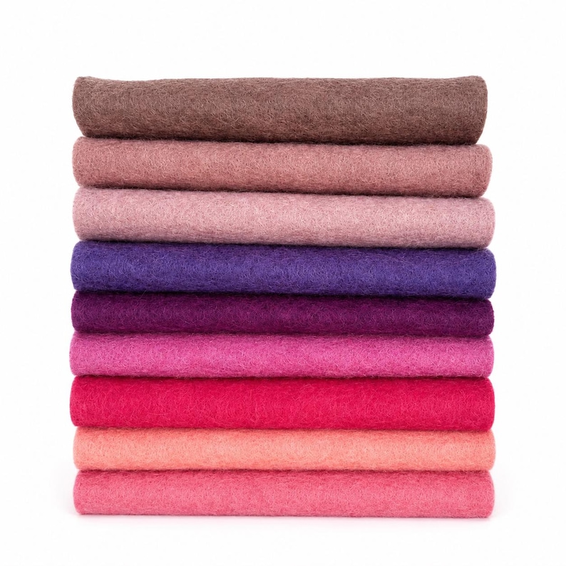 May include: A vertical stack of ten rectangular felt sheets in a gradient of colors, ranging from dark brown at the top, transitioning through shades of mauve, purple, and magenta, to a bright pink at the bottom, all featuring a textured surface.
