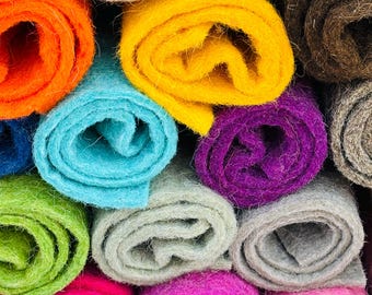 Könnte beinhalten: Eine Auswahl an bunten Filzrollen, darunter orange, gelb, blau, lila, grün, rosa und grau. Die Rollen sind übereinander gestapelt und bilden so ein optisch ansprechendes Display.