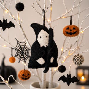 May include: A Halloween-themed display featuring felt ornaments hanging from white branches. Ornaments include a black Grim Reaper, jack-o'-lanterns, bats, spiderwebs, and black spheres. The scene is illuminated by small white lights, creating a festive atmosphere.