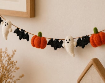 May include: A Halloween garland featuring felted figures strung on a thin brown cord. The sequence includes white ghosts with black eyes, black bats with outstretched wings, and bright orange pumpkins with green stems, alternating along the string.