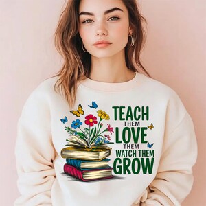 K&ouml;nnte beinhalten: Ein wei&szlig;er Pullover mit einem gr&uuml;nen, floralen Design und dem Text "Teach them love, watch them grow".