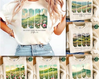 May include: Cream-coloured t-shirts and sweatshirts with a landscape design featuring a cross on a hill, flowers, and the text "HE IS NOT HERE. HE HAS RISEN Matthew 28:6". The design is repeated on multiple shirts.