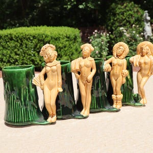 May include: A vintage ceramic planter featuring four nude female figures. The planter is dark green with a textured tree trunk design. The figures are tan and have elaborate headdresses.