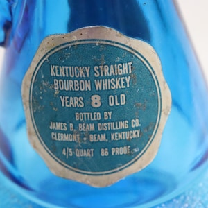 May include: Close-up of a blue glass bottle with a label that reads "Kentucky Straight Bourbon Whiskey Years 8 Old." The label also indicates the distiller and location. The bottle is 4/5 quart and 86 proof.