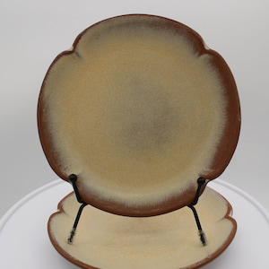 May include: A set of two ceramic plates with a scalloped edge. The plates are a light brown color with a speckled glaze. The plates are stacked on top of each other.