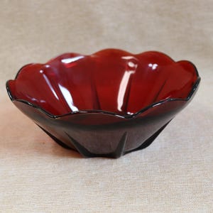 Peut inclure: Un bol en verre rouge foncé avec un bord festonné. Le bol a une finition brillante et une base sombre, presque noire. La forme rappelle une fleur. Ce bol décoratif convient au service ou à l'exposition.