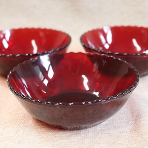 Pode incluir: Três tigelas de vidro vermelho rubi com bordas onduladas. As tigelas são redondas com um interior profundo e uma superfície texturizada. As tigelas estão dispostas em grupo, mostrando sua cor e design. Estas tigelas são adequadas para servir alimentos.