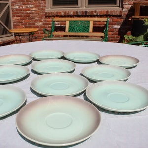May include: A set of ten light blue and white ceramic saucers with a subtle ombre effect. The saucers are arranged in a circle on a white tablecloth.