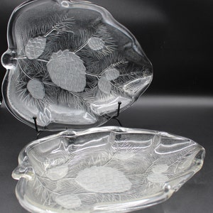 May include: Two clear glass serving dishes with an etched design of pine branches and pine cones. The dishes are stacked on top of each other.