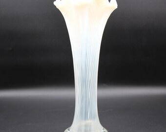 May include: A white opalescent glass vase with a ruffled top and a textured, ribbed design. The vase is tall and slender, with a flared base.