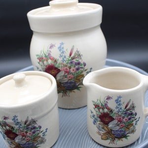 以下が含まれることがあります： 花柄の白いセラミック製の砂糖とクリームのセット。セットには、蓋付きの砂糖入れ、クリームピッチャー、トレイが含まれています。