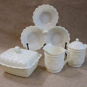 Pode incluir: Um conjunto de pratos de servir brancos em estilo vintage. O conjunto inclui um prato de servir de três secções, um prato quadrado com tampa, um cremeira e um açucareiro com tampa. Todas as peças têm um padrão texturizado.