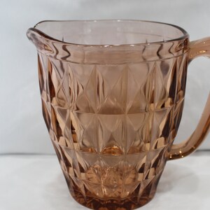 Op de afbeelding: Een vintage glazen kan met een diamantpatroon. De kan is lichtroze van kleur en heeft een handvat.