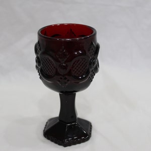 Op de afbeelding: Een donkerrode glazen kelk met een zeshoekige voet en een decoratief patroon rond de bovenkant.