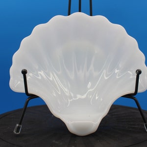 May include: White milk glass shell-shaped dish. The dish is on a black stand.