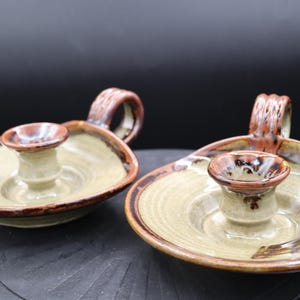Könnte beinhalten: Zwei Kerzenhalter aus Keramik mit brauner und grüner Glasur. Jeder Halter hat eine einzelne Kerzenaufnahme und einen Griff.