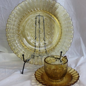 May include: A set of amber glass dishes, including a large plate, a saucer, and a cup. The dishes have a delicate, embossed pattern and a vintage look.