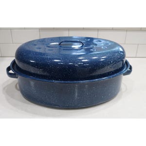 May include: An oval-shaped roasting pan with a matching lid, featuring a dark blue enamel finish with a white speckled pattern. The roaster includes two side handles and a central handle on the lid, constructed from durable metal materials.