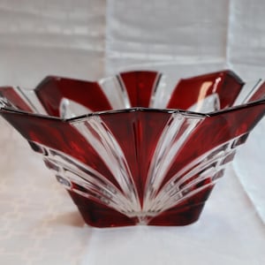 May include: A decorative glass bowl with a striking design. The bowl features a deep red color on the outer edges, transitioning to clear glass with a fan-like pattern. The bowl has a square base and a scalloped rim.