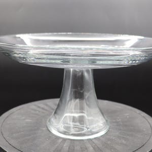 Può includere: Un alzatina per torte in vetro trasparente con un piatto largo e poco profondo e una base a piedistallo svasata. L'alzatina è realizzata in vetro trasparente, che consente il passaggio della luce. L'alzatina per torte è progettata per esporre prodotti da forno.