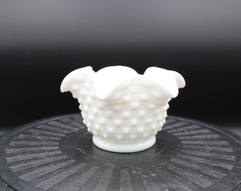 May include: A white milk glass bowl with a ruffled edge and a dotted texture. The bowl is sitting on a black surface.