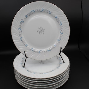 May include: A set of ten white dinner plates with a blue and silver floral pattern around the rim. The plates are stacked on top of each other.
