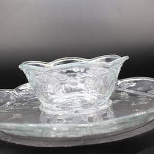 May include: A clear glass serving dish with a scalloped edge and a matching bowl. The dish and bowl have a delicate floral pattern.