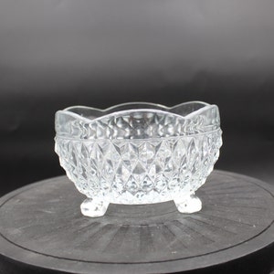 May include: A clear glass bowl with a diamond pattern and three legs. The bowl is on a black surface.