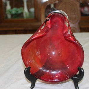 Może przedstawiać: Czerwona szklana miska o falistym, organicznym kształcie. Miska stoi na czarnym stojaku.