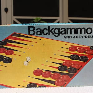 May include: A vintage Milton Bradley Backgammon and Acey-Deucy game box. The box features a colorful illustration of a backgammon board with red and black game pieces.