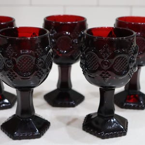 Könnte beinhalten: Ein Set aus fünf tiefroten Glas-Kelchen mit einem texturierten geometrischen Muster auf der Kuppa, einem dicken Stiel und einem sechseckigen Fuß. Das Glasgeschirr hat einen einheitlichen dunklen Rubin-Farbton und ein geprägtes Muster.