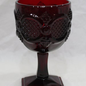 Könnte beinhalten: Ein rubinroter Glasbecher mit einem Rautenmuster auf der Schale und einem geometrischen Fuß. Der Stiel hat eine rechteckige Form. Der Becher dient zum Servieren von Getränken.